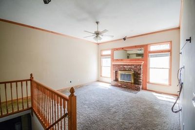 Unfurnished living room featuring ceiling fan, a wealth of natural light, a brick fireplace, and carpet flooring | Image 3