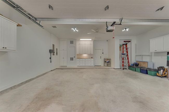 The oversized garage is equipped with built-in cabinets along three walls, offering abundant closed storage, as well as a dedicated work space with additional cabinetry. Notable features include an insulated garage door, a WiFi-enabled LiftMaster opener, and 5/8" sheetrock walls insulated with Rockwool for sound and fire resistance. A solid garage door between the garage and the main living space for added safety. | Image 38