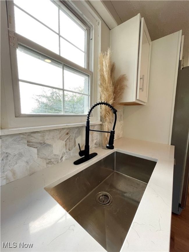 Kitchen view of backsplash, light stone counters, freestanding refrigerator, and white cabinets | Image 8