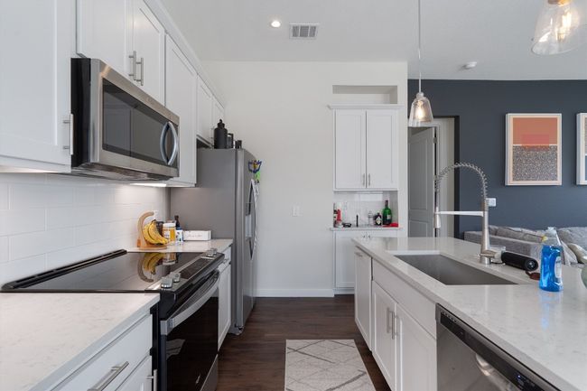 Kitchen featuring stainless steel appliances, decorative backsplash, white cabinets, dark wood-style floors, and light stone countertops | Image 23