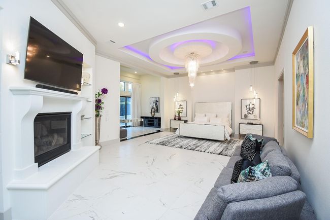 This elegant bedroom features a sophisticated feature ceiling with ambient lighting and a stunning chandelier, fireplace and large sitting area. | Image 22
