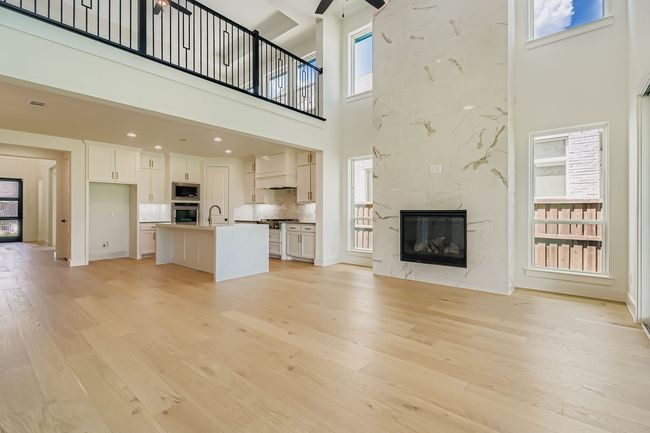 Unfurnished living room featuring a high end fireplace, light wood-style floors, and a towering ceiling | Image 5