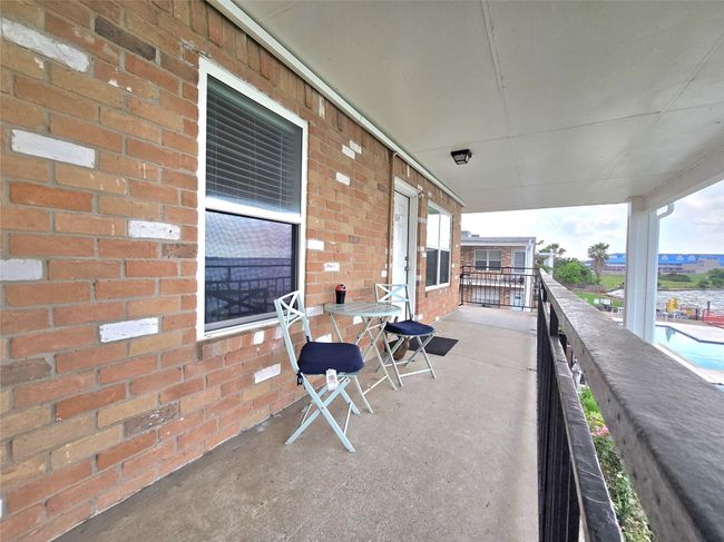 This photo showcases a spacious, covered balcony with a cozy seating area and views of a pool. The brick exterior adds charm, and there's ample room for outdoor relaxation. | Image 21