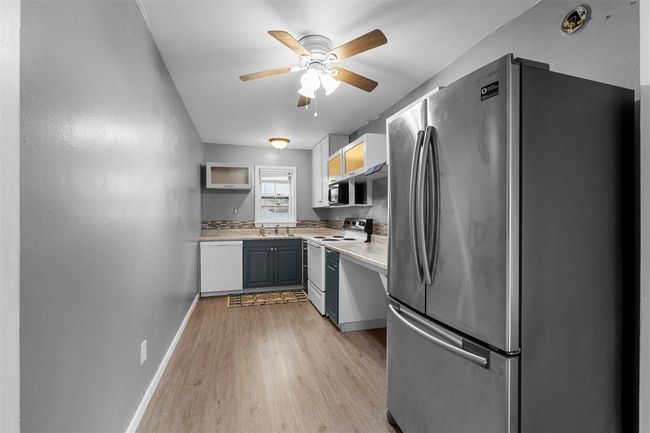 Kitchen featuring a sink, ceiling fan, white appliances, light wood-style flooring, and light countertops | Image 7