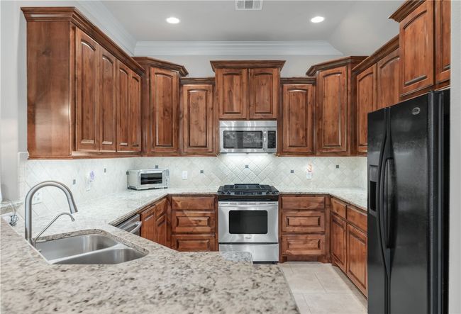 Kitchen featuring appliances with stainless steel finishes, a sink, ornamental molding, light stone countertops, and decorative backsplash | Image 11