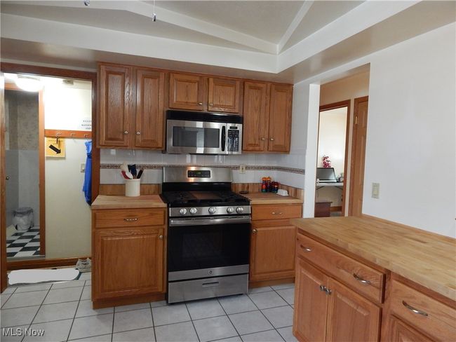 Kitchen with light ceramic tile floors, stainless steel appliances, butcher block counters, vaulted ceiling, solid Oak cabinetry (2024) & Ceiling Fan. | Image 9