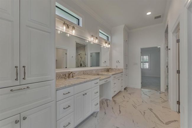 The primary bath serves as a stylish and functional connection between the two primary bedrooms. It features double sinks, a dedicated vanity area, and custom cabinetry—all topped with elegant Cambria quartz countertops. Floor-to-ceiling cabinets provide ample storage and include a built-in laundry hamper that can be easily converted to shelving, offering flexibility to suit your needs. | Image 23