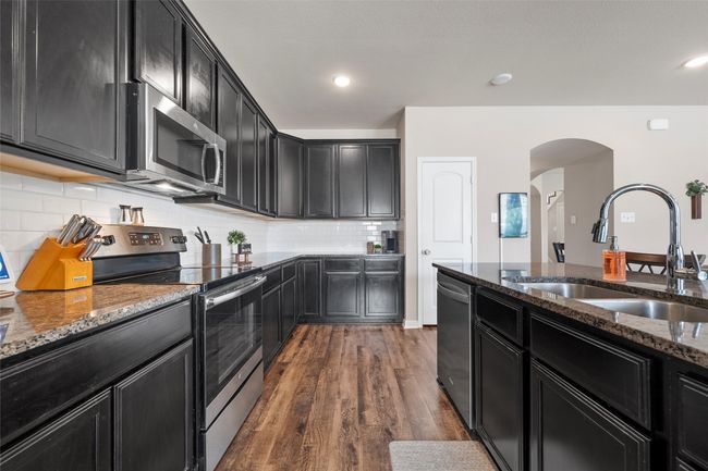 Kitchen featuring stainless steel appliances, dark cabinets, arched walkways, and dark stone counters | Image 5