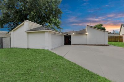 Single-story suburban home with a beautiful facade, generous driveway area, and a well-manicured lawn under a twilight sky. | Image 1