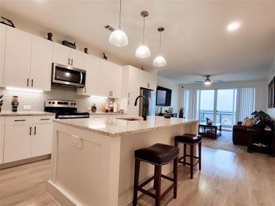 Kitchen with light hardwood / wood-style flooring, pendant lighting, appliances with stainless steel finishes, an island with sink, and ceiling fan | Image 1