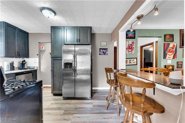 Kitchen featuring appliances with stainless steel finishes, light wood-style floors, a textured ceiling, a kitchen breakfast bar, and backsplash | Image 13