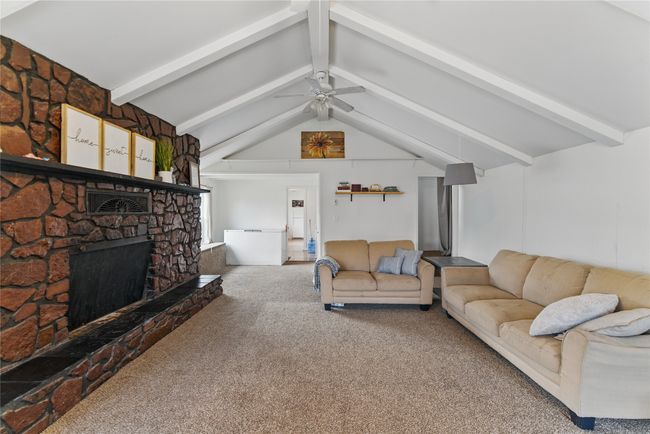 Carpeted living area with lofted ceiling with beams, a fireplace, and ceiling fan | Image 12