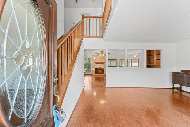 This welcoming entryway features a decorative glass door leading into a bright, open living space with hardwood floors and a staircase. The area is accented by an overlook and built-in shelving, providing a warm and inviting atmosphere. | Image 10