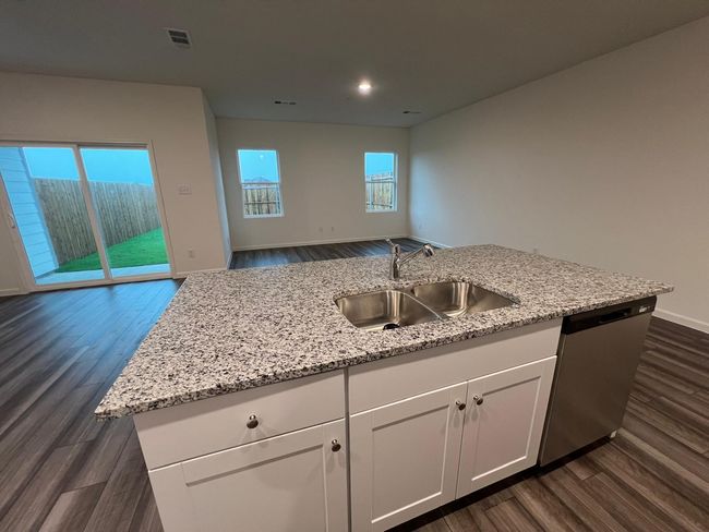 Kitchen with a sink, dishwasher, open floor plan, dark wood-type flooring, and light stone countertops | Image 6