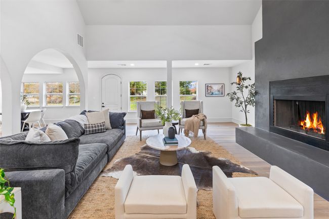 Living area featuring light wood-style floors, a high ceiling, healthy amount of natural light, a warm lit fireplace, and arched walkways | Image 23