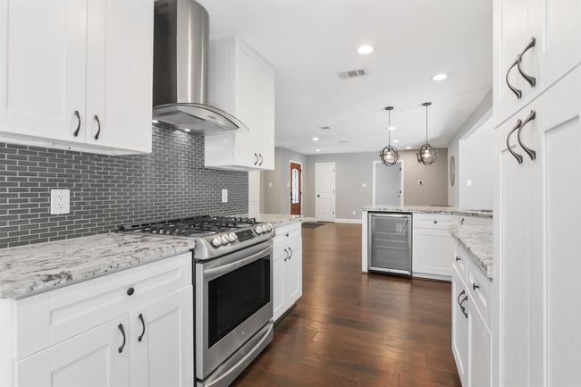 This updated kitchen is perfect for the chef in the family. It features matching stainless steel appliances to include a gas range and wine fridge. The granite countertops flow seamlessly into the decorative tile backsplash for a clean sleek look. | Image 12