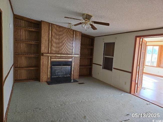 Unfurnished living room featuring a textured ceiling, a glass covered fireplace, a ceiling fan, carpet floors, and built in features | Image 29