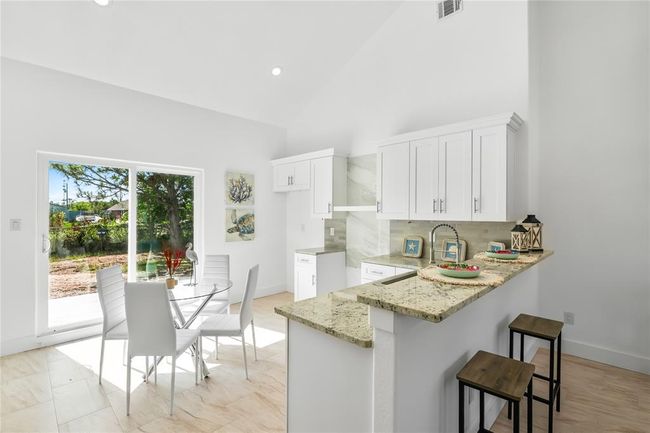 Bright and airy kitchen featuring sleek white cabinetry, a stylish breakfast bar, and abundant natural light from large sliding doors that open to a scenic view. Ideal for both everyday meals and entertaining. | Image 9