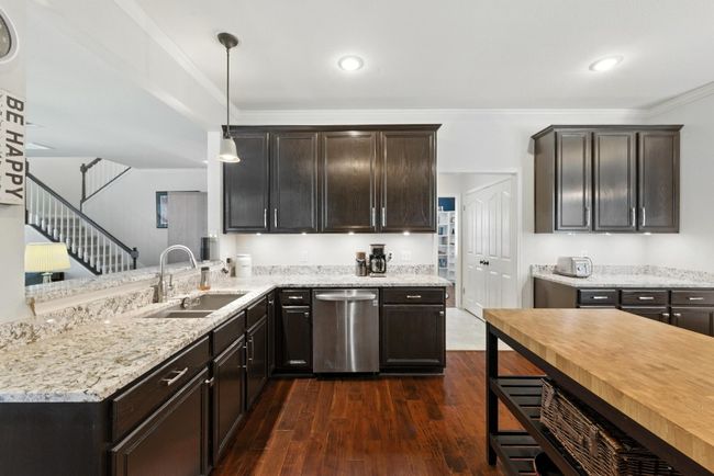 Kitchen featuring stainless steel dishwasher, dark wood-style floors, light stone counters, pendant lighting, and dark brown cabinets | Image 11