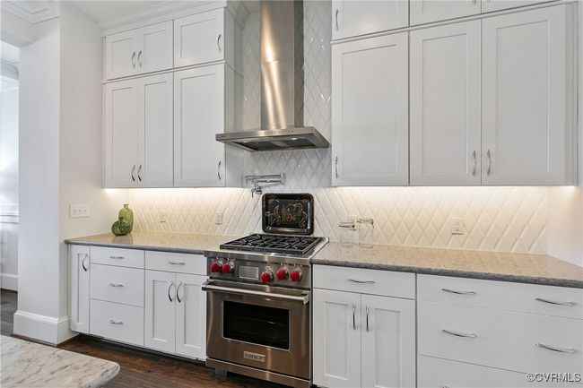 Kitchen with white cabinetry, wall chimney range hood, premium stove, backsplash, and light stone countertops | Image 9