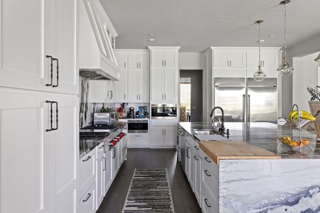 Kitchen featuring custom range hood, dark wood-style floors, white cabinetry, stainless steel appliances, and a sink | Image 9