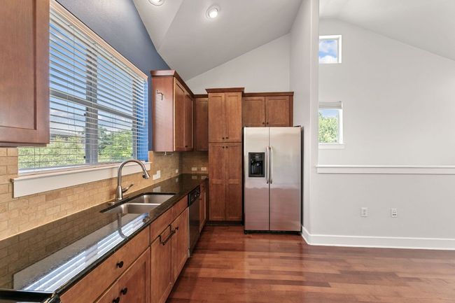 Kitchen featuring stainless steel appliances, dark stone counters, dark wood-type flooring, vaulted ceiling, and tasteful backsplash | Image 13