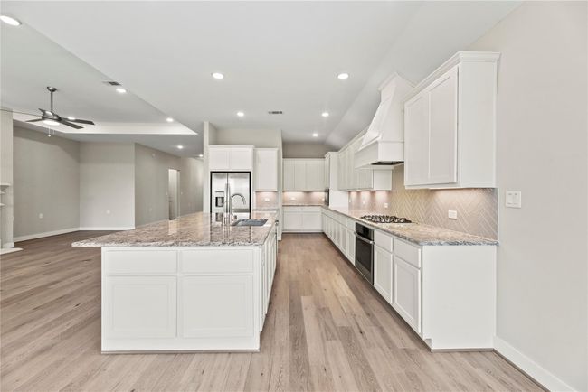This chef-inspired kitchen is both stylish and functional, featuring an expansive island with bar seating and cabinets on four sides below, granite countertops, herringbone tile backsplash highlighted by under-cabinet lighting, and crisp white cabinetry. With stainless steel appliances, a walk-in pantry and abundant prep space, it’s ready to handle everything from weeknight meals to holiday feasts. | Image 14