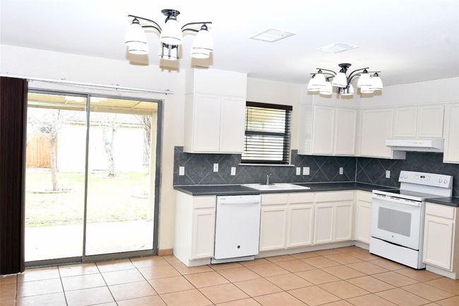 Kitchen with under cabinet range hood, white appliances, a sink, dark countertops, and an inviting chandelier | Image 8