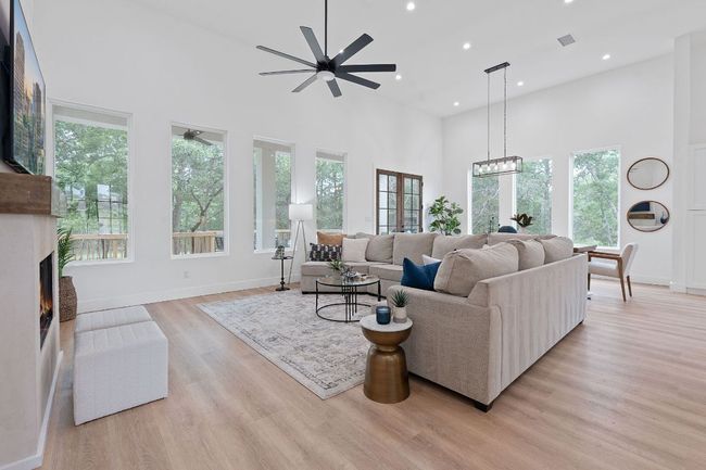 Living room featuring a high ceiling, a lit fireplace, ceiling fan with notable chandelier, and a wealth of natural light | Image 5