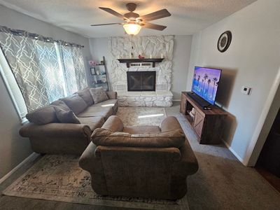 Carpeted living room featuring ceiling fan, a stone fireplace, and a textured ceiling | Image 3