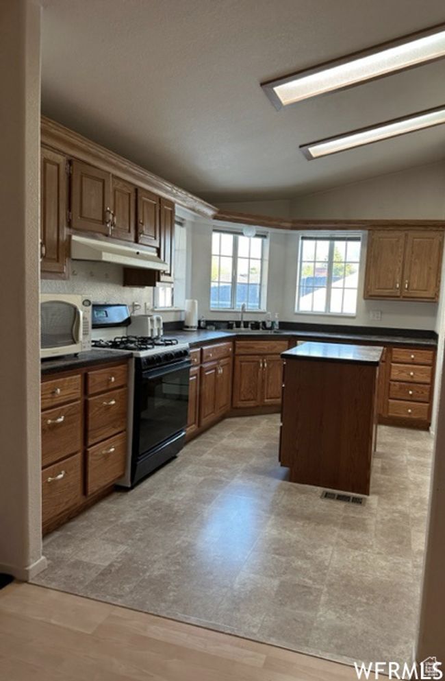Kitchen with black gas stove, visible vents, stainless steel microwave, and dark countertops | Image 7