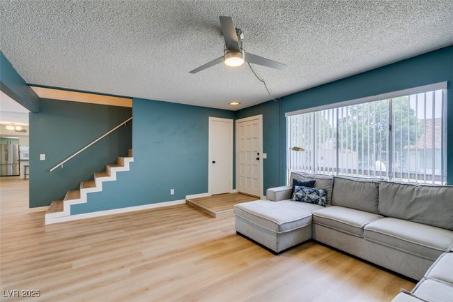 Living area with a textured ceiling, ceiling fan, wood finished floors, and stairs | Image 9
