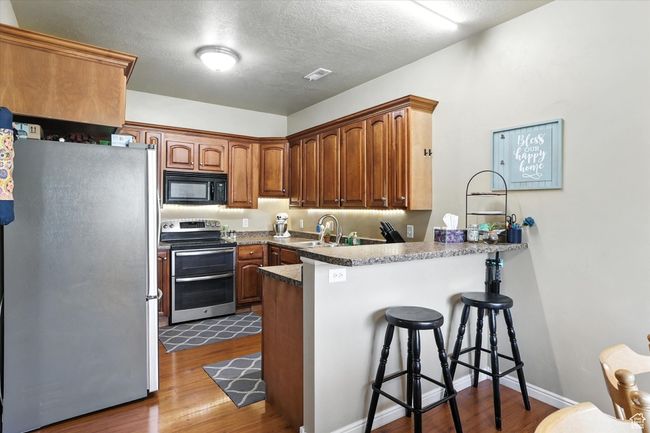 Kitchen with appliances with stainless steel finishes, a peninsula, a kitchen breakfast bar, dark wood-type flooring, and a textured ceiling | Image 10