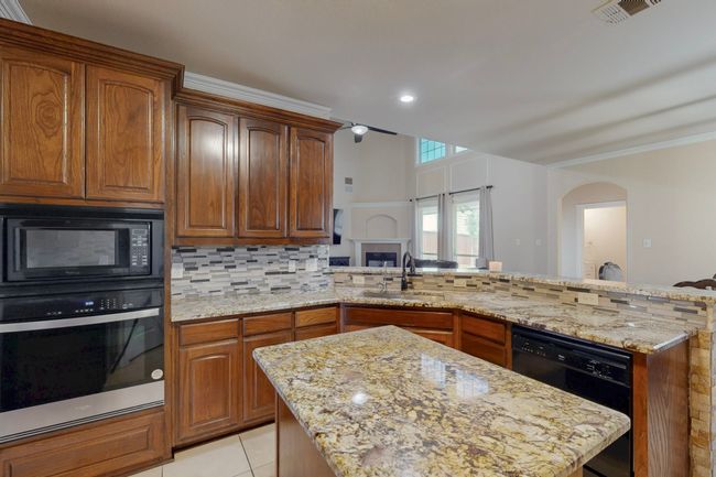 Kitchen featuring a sink, black appliances, decorative backsplash, light stone countertops, and visible vents | Image 9