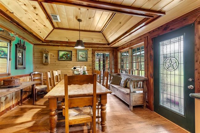 This cozy dining area features rustic wood paneling, a wooden table and chairs, and large windows providing ample natural light. The space is complemented by a decorative glass door and a bench for additional seating, creating a warm and inviting atmosphere. | Image 20