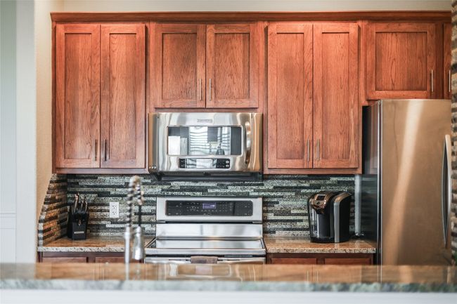 Kitchen featuring brown cabinetry, stone countertops, tasteful backsplash, and appliances with stainless steel finishes | Image 8
