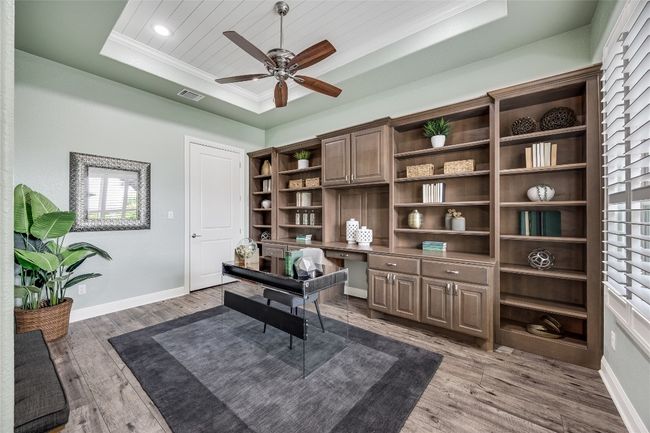 Office area with a raised ceiling, wood finished floors, crown molding, a ceiling fan, and built in desk | Image 15