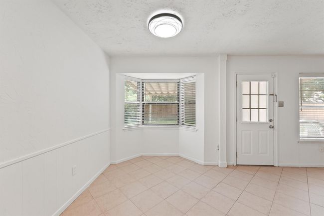 Bright room with tiled floors, a bay window, and a door leading outside. Neutral walls and ceiling with a modern light fixture. | Image 12