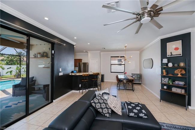 Living room with light tile patterned floors, crown molding, ceiling fan with notable chandelier, and visible vents | Image 5
