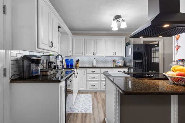 Kitchen featuring black appliances, extractor fan, white cabinets, light wood-type flooring, and crown molding | Image 8