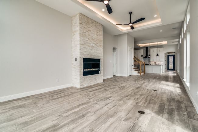 Unfurnished living room with a tray ceiling, a fireplace, ceiling fan, and light hardwood / wood-style flooring | Image 4