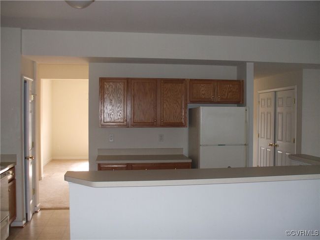 Kitchen with freestanding refrigerator, brown cabinets, dishwasher, light colored carpet, and light flooring | Image 4