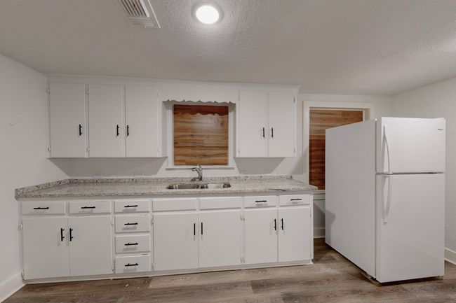 Kitchen with white refrigerator, sink, white cabinets, and light wood-type flooring | Image 12