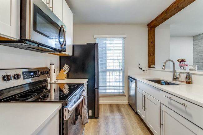 Kitchen with a sink, light wood-type flooring, white cabinetry, light countertops, and appliances with stainless steel finishes | Image 8