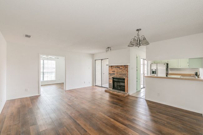 Unfurnished living room featuring a chandelier, dark wood-style flooring, a brick fireplace, and a ceiling fan | Image 4