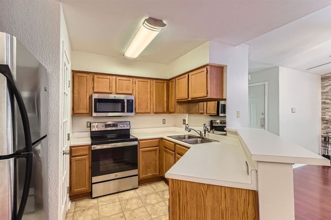 Kitchen featuring stainless steel appliances, a peninsula, light countertops, large pantry (door on left) and wood cabinetry | Image 7