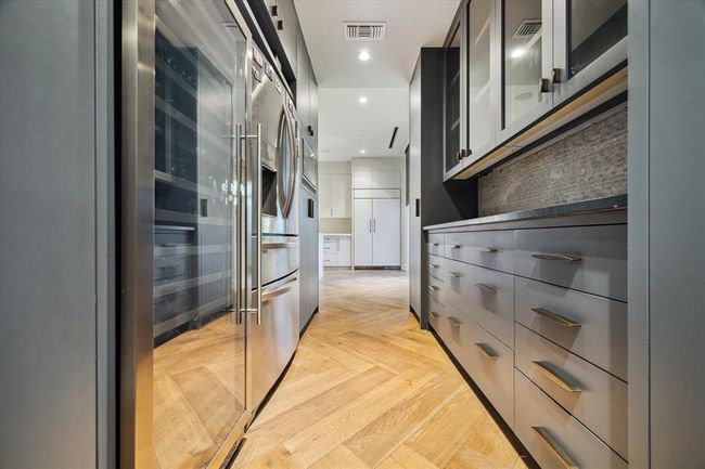 On the opposite side, a long countertop serves as the perfect spot for a coffee station, toaster setup, or bar area. Glass-front upper cabinets, three banks of drawers, and floor-to-ceiling storage offer both beauty and utility. And just ahead? The built-in main refrigerator, seamlessly integrated into the cabinetry for a clean, elevated look. | Image 13