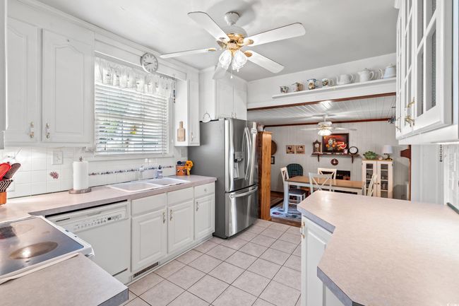 Kitchen featuring ceiling fan, stainless steel fridge, light countertops, and wood walls | Image 6