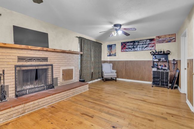 Unfurnished living room with a brick fireplace, ceiling fan, wood finished floors, and wainscoting | Image 22