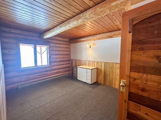 Empty room with rustic walls, a baseboard heating unit, dark colored carpet, wooden ceiling, and beamed ceiling | Image 37